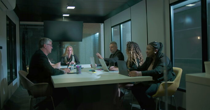 Team of professionals engaged in collaborative meeting around modern boardroom table, using laptops and colorful stationery, corporate office environment - Powered by Adobe