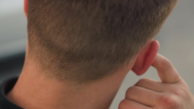 young man removing earbud behind ear with closeup on nape and fingers, outdoor postworkout vibe, casual short haircut, motion of pulling and relief, wireless audio gadget detail, candid cool-down