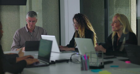 Team working independently on laptops in modern office meeting room with digital display and collaborative environment
