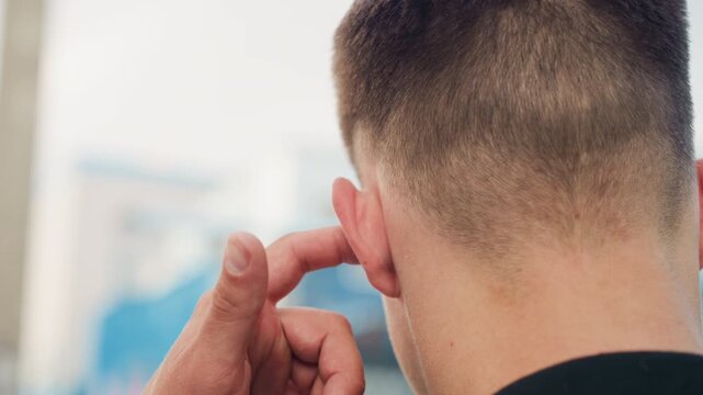 young man inserting earplug close-up. hands adjusting foam plug at ear, short haircut, blurred urban background, routine preparation for noisy environment, worker commuter musician contexts, safety