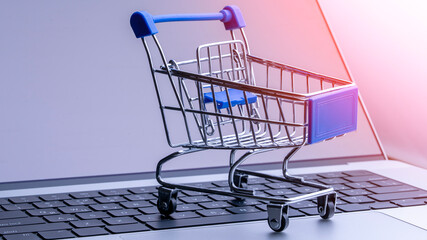 A shopping cart is displayed on a laptop keyboard. The cart is made of metal and has a blue handle. The laptop is open and the keyboard is visible