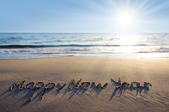 Happy New Year lettering on the sunny beach sand.