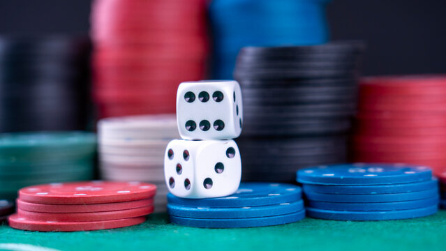 Two dice are on top of a pile of poker chips. The chips are of different colors and sizes, and the dice are white. Concept of excitement and anticipation