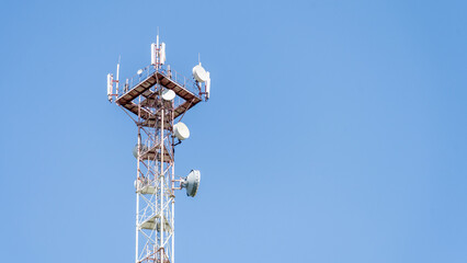 A tall tower with many antennas on top. The sky is clear and blue. The tower is a cell phone tower