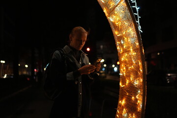 Woman using smartphone near festive lights