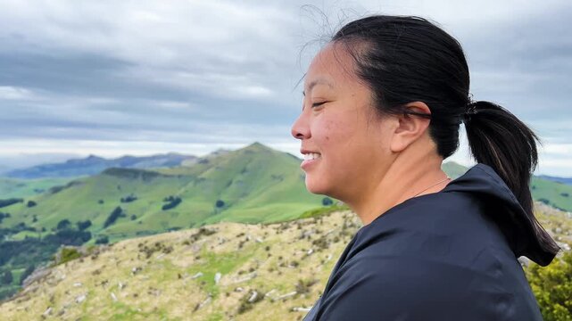 Asian woman smiling on Montgomery Peak, Akaroa Peninsula, embracing nature, close up