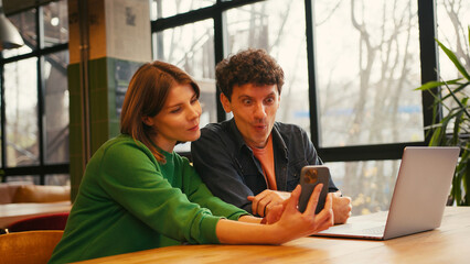 Couple, woman holding mobile phone using mobile app sitting in modern coworking