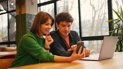 Couple, woman holding mobile phone using mobile app sitting in modern coworking