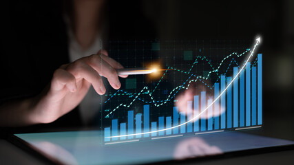 A business professional interacts with a digital graph on a tablet, showcasing rising trends and financial data in a modern workspace setting. Impute