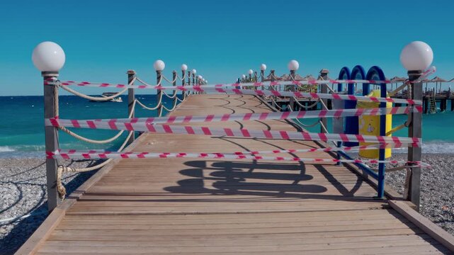 The pier is closed to vacationers due to rough seas and strong winds. Waves crash against the breakwaters, and the strips of the pier flutter and sway in the gusts of wind. The deserted shore and stor
