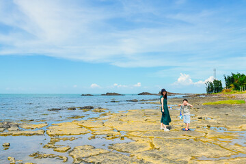 One Asian mom and her boy enjoying the beautiful volcanic rock landform coastline landscape of Leigong Island in Chengmai County, Hainan, China, in autumn season	