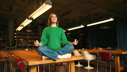Fotobehang Lotusbloem Relaxed young woman meditating in lotus position on table in modern coworking  © RZ Images