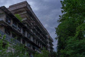 Abandoned concrete hotel above dense forest under overcast sky