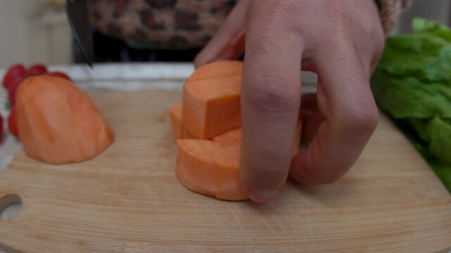 A man cuts peeled sweet potato into slices on a wooden cutting board. Healthy eating. Close-up.