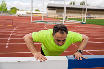 Determined senior athlete doing push-ups on track hurdle at stadium