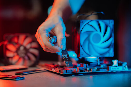 system administrator installing SSD into motherboard, assembling PC of different accessories or components, close-up view of hands, computer repair and maintenance concept