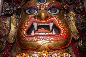 Large ceremonial guardian deity mask at a Kathmandu temple in Nepal, with gold and red detailing, offerings, and traditional Newar craftsmanship.