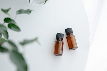Two amber essential oil bottles on white table with green plant, minimal natural light