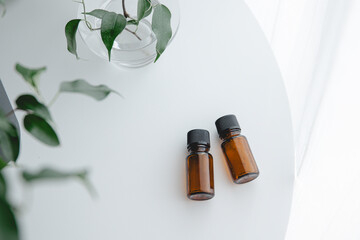 Two amber essential oil bottles on white table with green plant, minimal natural light