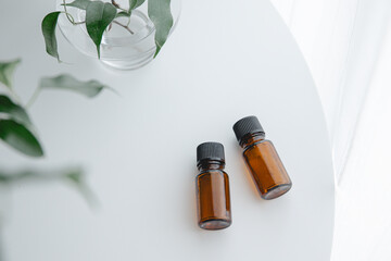 Two amber essential oil bottles on white table with green plant, minimal natural light