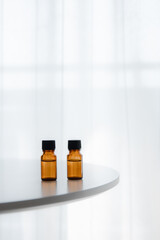 Amber essential oil bottles on round white table by bright window, vertical minimal background