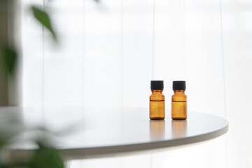 Two amber essential oil bottles on white table with soft greenery, horizontal copy space