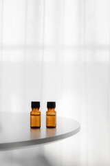 Amber essential oil bottles on round white table by bright window, vertical minimal background