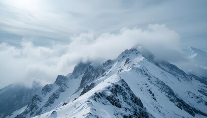 Snowcovered mountain peaks shrouded in lowhanging clouds under bright sky