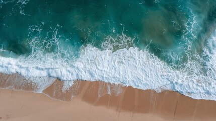 An aerial view of the ocean meeting the sandy beach with beautiful color variations