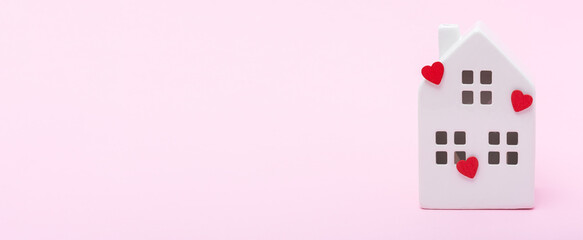 White ceramic house model adorned with red heart decorations on a soft pink background, symbolizing love, warmth, and the concept of home and family togetherness