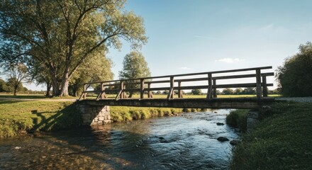Rustic wooden bridge spans a shallow stream through a parkland setting.  Sunlight filters through trees