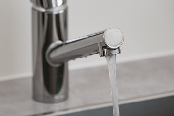 Water flowing from a modern chrome faucet into a kitchen sink