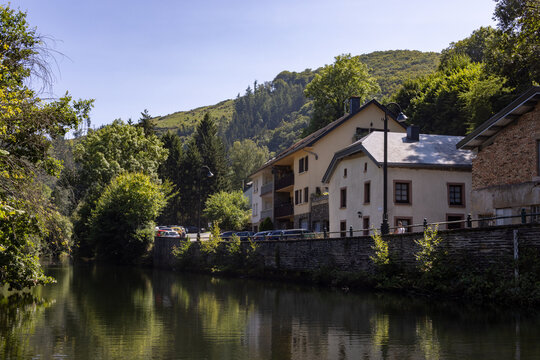 Esch-sur-Sure, Wiltz, Grand-Duche de Luxembourg, September 07, 2025, Peaceful scene with houses by flowing water, Calm river reflecting houses with sunny facades and surrounding lush trees