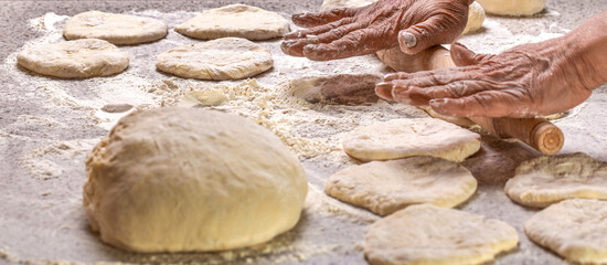 Old woman hands hands keep rolling pin with flour on table. Woman rolling out dough on kitchen table, closeup