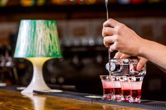 Shots at the nightclub. Barman preparing cocktail shooter. Bartender pouring strong alcoholic drink into small glasses on bar