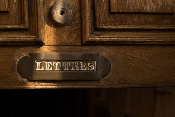 Vintage French mail slot 'LETTRES' on aged wooden door with brass plate and warm sunlit patina
