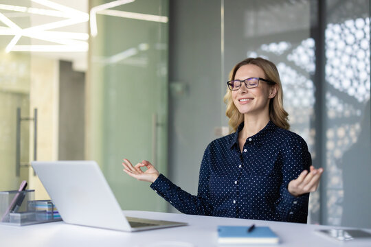 Businesswoman practicing mindfulness meditation at her modern office desk, finding peace and relieving stress with closed eyes and a serene expression, promoting mental wellness during work breaks
