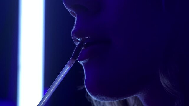 Close up of a woman applying lip gloss in a dark room lit by blue neon light