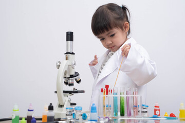 A young child in a white lab coat exploring colorful liquids in test tubes with a microscope, representing early science education, creativity, and curiosity in a modern learning environment.