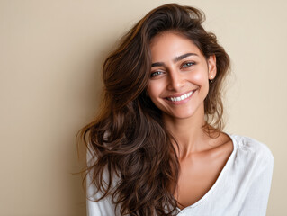 Naklejka premium Smiling young woman with long brown hair wearing white shirt against beige background, natural beauty and happiness