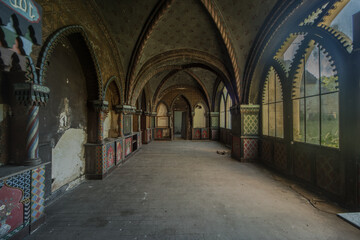 Obraz premium Abandoned Gothic Chateau Interior with Ornate Arches, Painted Panels and Sunlit Arched Windows