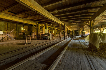 Fototapeta premium Abandoned Sawmill Interior with Vintage Machinery and Sunlit Wooden Beams