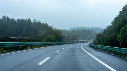 A smooth highway with green guardrails and lush trees on both sides