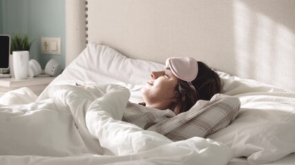 Young woman with sleep mask resting peacefully in a cozy bed, surrounded by soft pillows and blankets, creating a serene atmosphere for relaxation and rejuvenation