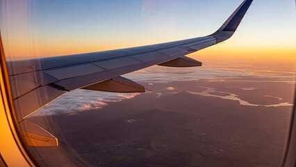 Airplane wing view from window during beautiful sunset or sunrise with clouds and land below