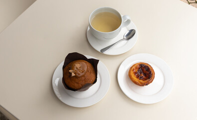 Coffee break with caramel muffin, pastel de nata and cup of green tea on table at cafe, top view