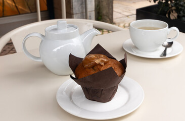 Caramel muffin, teapot, cup of tea on table at cafe. Cozy cafe atmosphere, soft natural lighting, and minimalist table setting