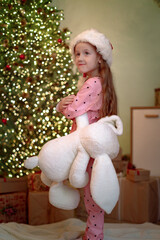 A little girl looks at the Christmas tree during the Christmas holidays and waits for gifts
