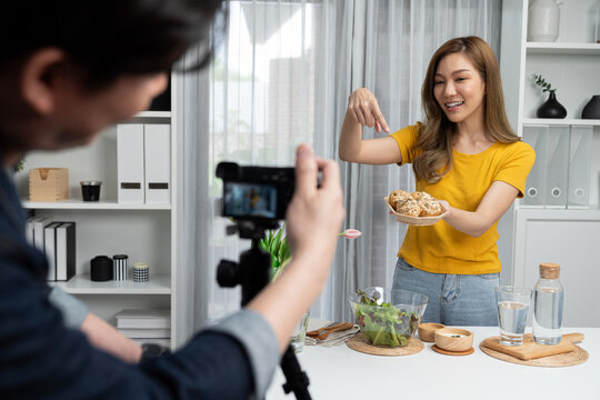 Asian beautiful woman food specialist presenting healthy meal wholegrain bun bread basket on live channel recorded video camera by smart cameraman streaming lifestyle social media online. Infobahn.