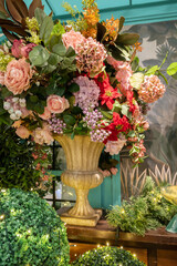 Luxurious indoor floral centerpiece featuring pink roses, soft hydrangeas, and vibrant greenery arranged in a golden urn.
